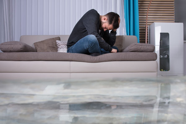 Flooded house with man sitting on couch that is upset